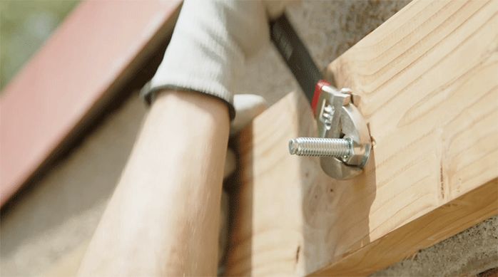 una persona aprieta la tuerca de un perno de expansión para fijar la viga principal del cobertizo de madera.