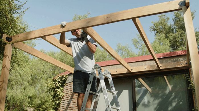 una persona fija las vigas secundarias del cobertizo de madera usando ángulos de acero galvanizado.