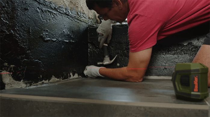 un hombre pone un clavo en el la parte inferior del muro de la ducha.