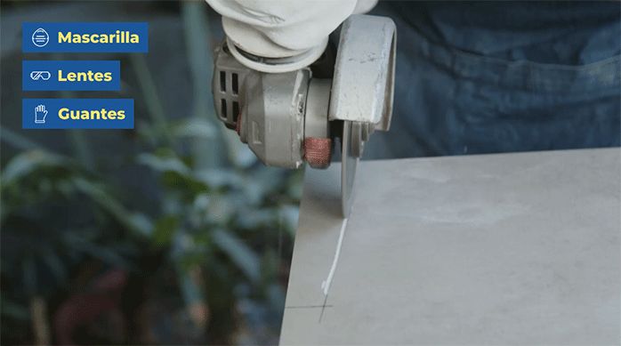 una persona usa un esmeril con disco de corte para hacer un corte irregular en una palmeta de porcelanato.