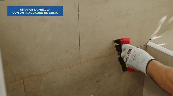 una persona usa un fraguador de goma para esparcir y alisar el fragüe en las junturas de las palmetas de porcelanato.