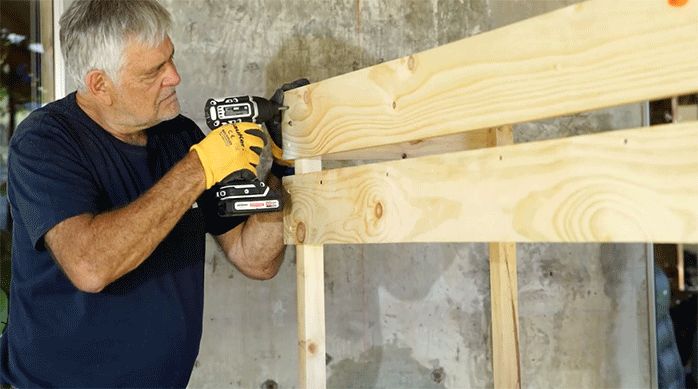 un hombre fija una tabla de pino seco cepillado para revestir la estructura de la jardinera movible.