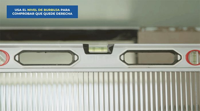 una persona pone un nivel de burbuja en la parte superior de una mampara para comprobar que está bien nivelada.