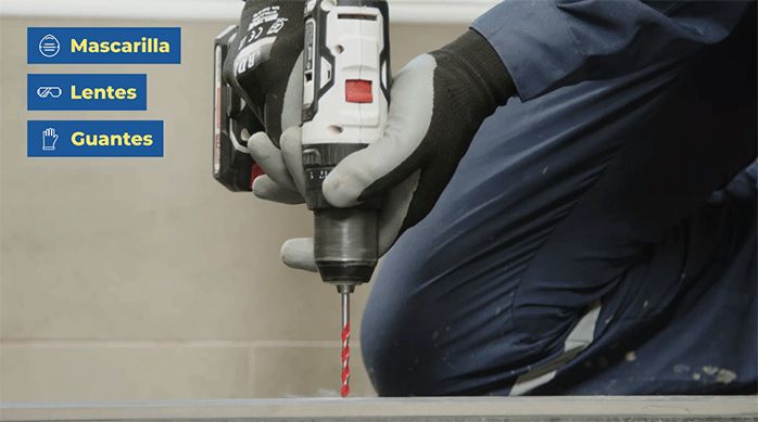 una persona perfora el piso del baño con un taladro y una broca, para instalar la mampara de ducha.