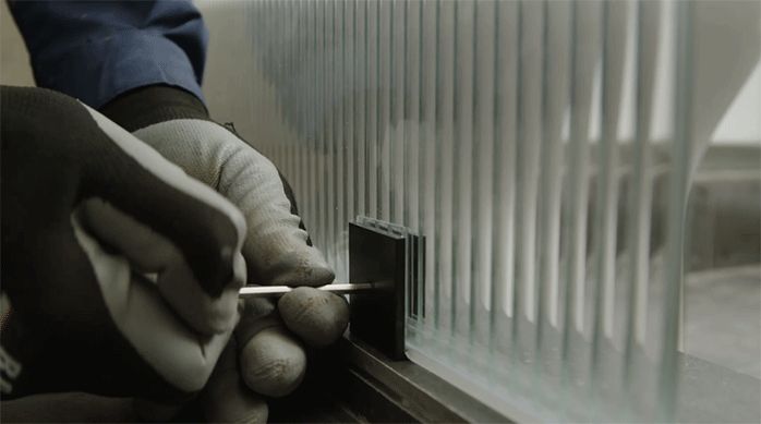 una persona fija la mampara de ducha en los herrajes de metal usando una llave allen.