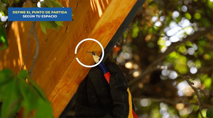 una persona marca el lugar de fijación de la persiana de bambú en la viga de madera usando un lápiz.