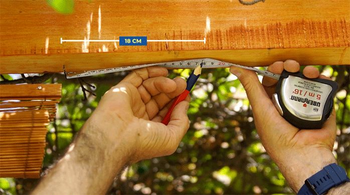 una persona marca el lugar de fijación de la segunda cortina de bambú usando una huincha de medir y un lápiz.