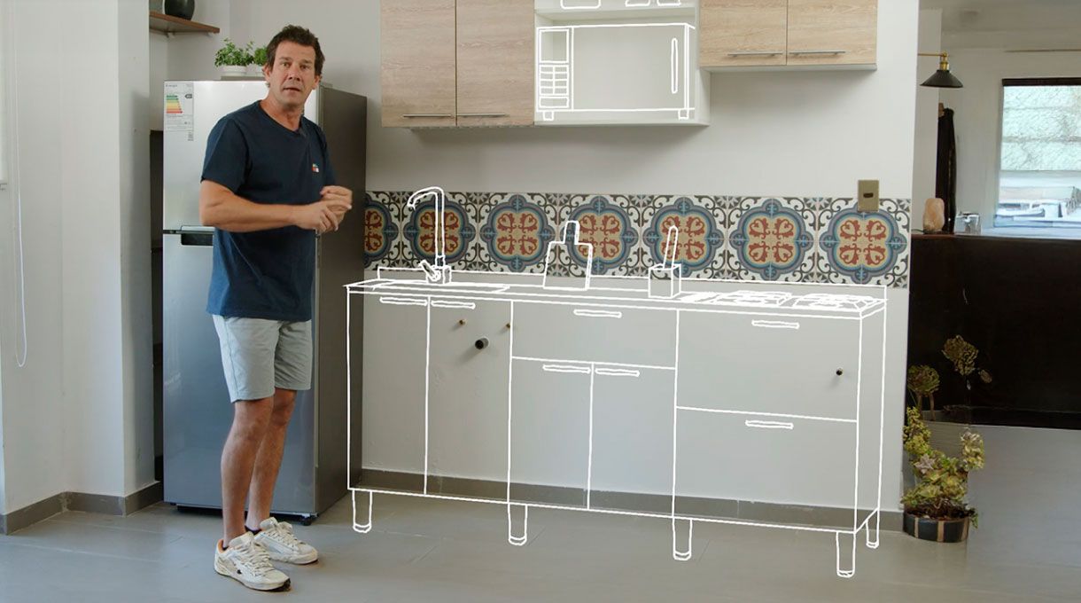 un hombre en una cocina pequeña junto a una gráfica que muestra cómo quedará el mueble con lavaplatos y encimera.