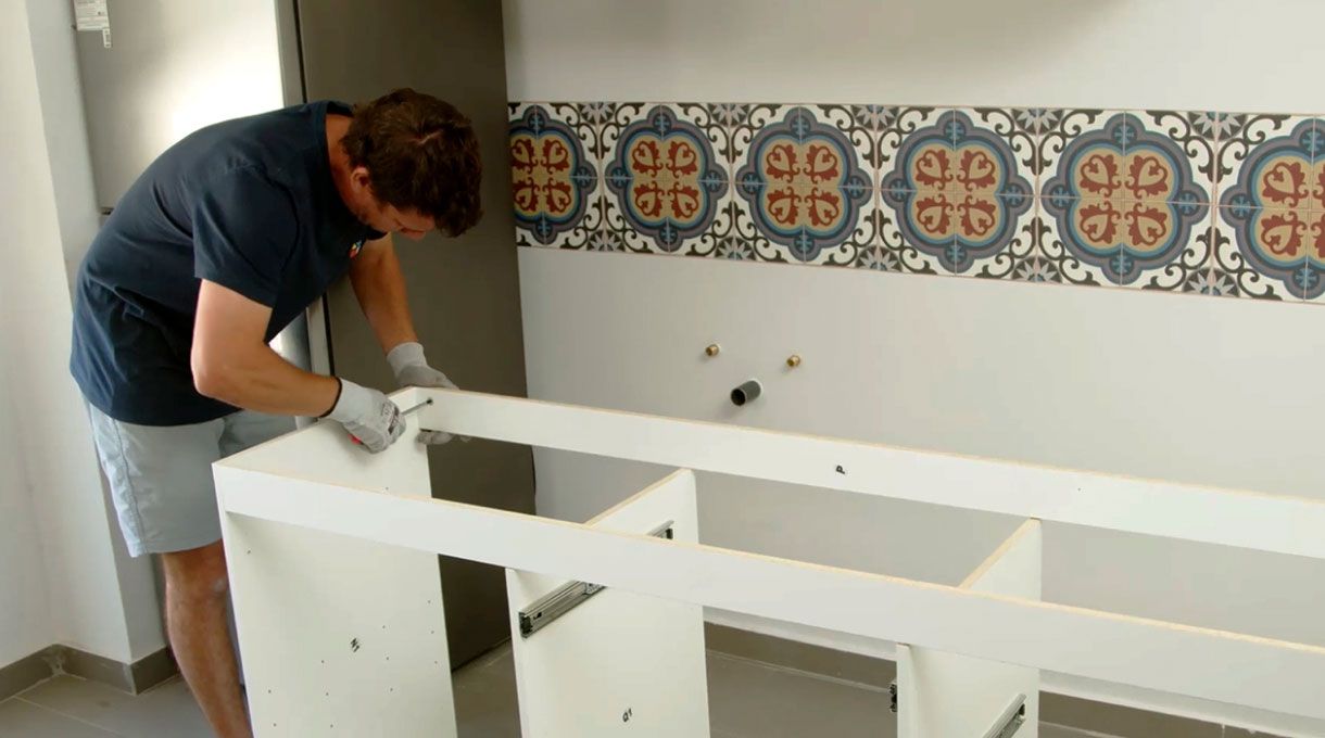 una persona fija el dintel del mueble con lavaplatos y encimera.