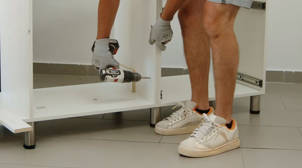 una persona atornilla los refuerzos interiores del mueble de cocina con lavaplatos y encimera.