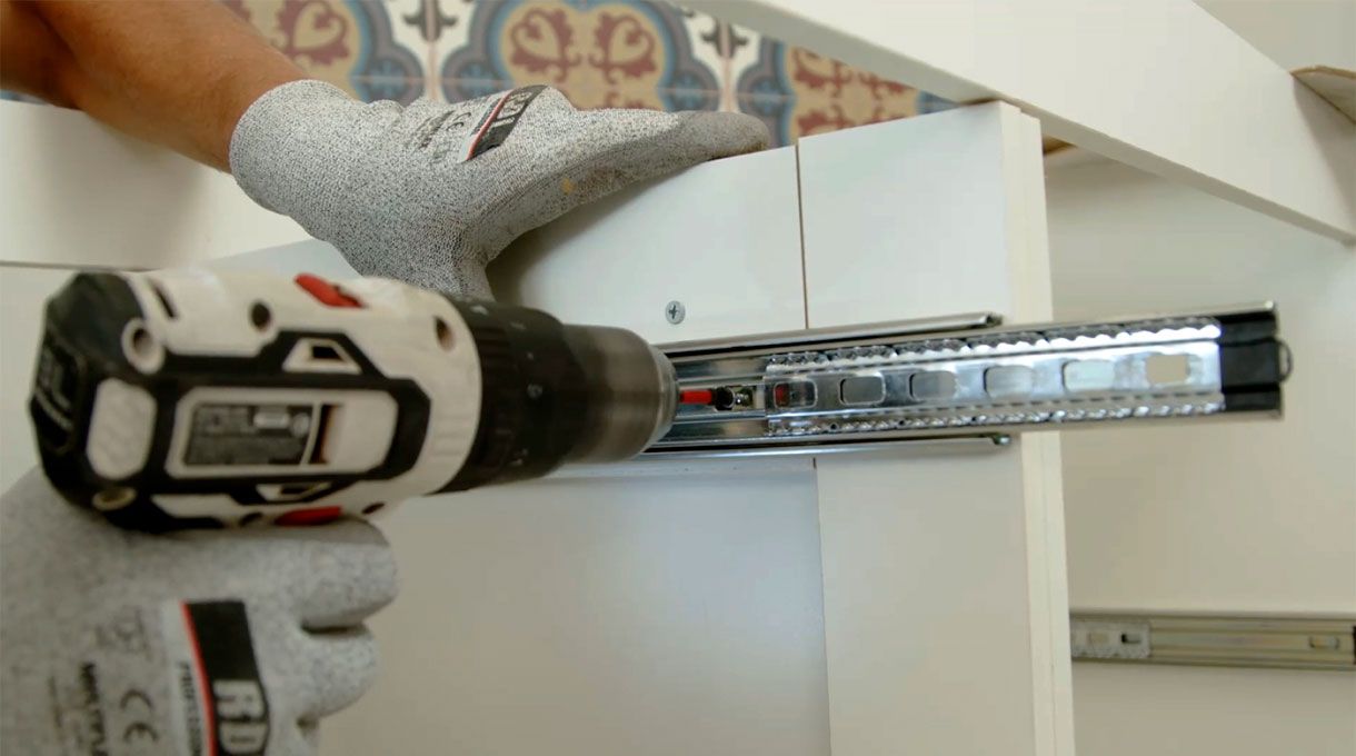una persona fija el riel o corredera en un vertical interior del mueble con lavaplatos y encimera.