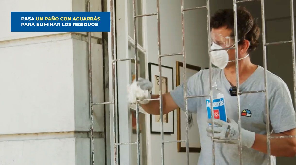 una persona con elementos de seguridad pasa un huaipe con aguarrás en una reja metálica de ventana.