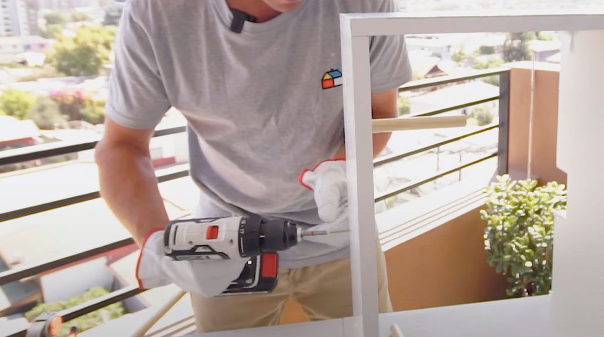 un hombre fija un trozo de barra de madera para cortina en la base del mueble organizador para cables.