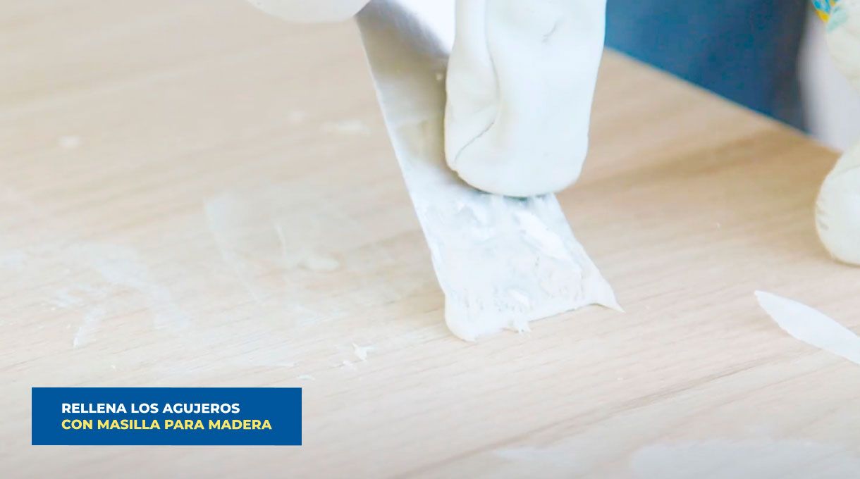 un hombre aplica pasta de retape con una espátula en las imperfecciones de un mueble de cocina.