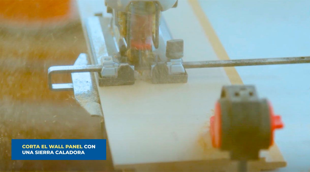 una persona corta un trozo de wall panel usando una sierra caladora.