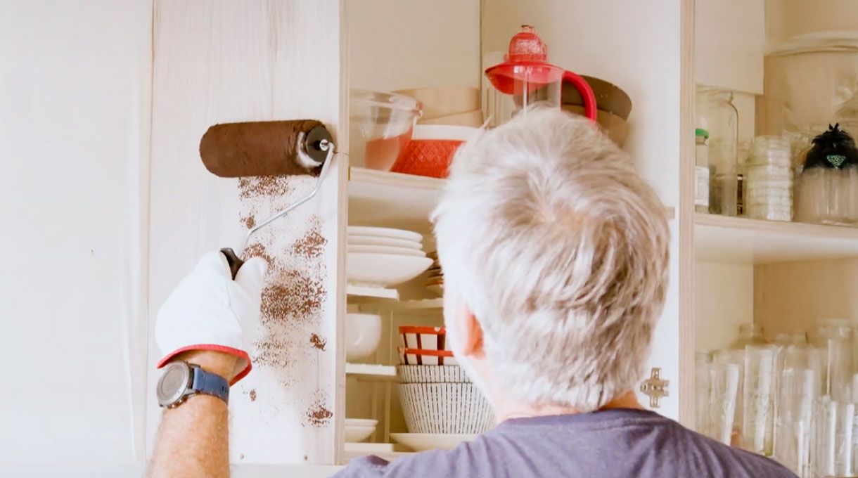 un hombre mayor pinta un mueble de cocina con pintura especial para melaminas, usando un rodillo esponja.