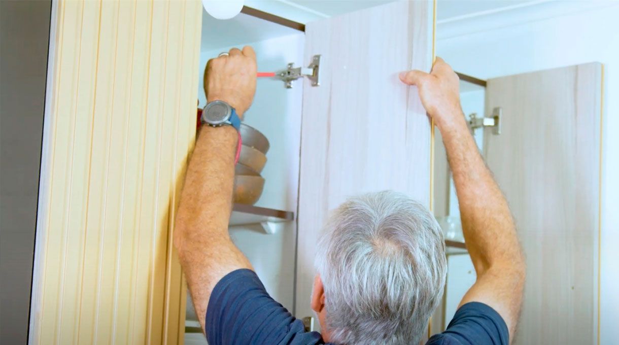 un hombre fija la puerta renovada del mueble de cocina.