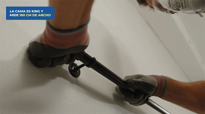 una persona encaja la barra de cortina en los soportes que instaló en el muro del dormitorio.