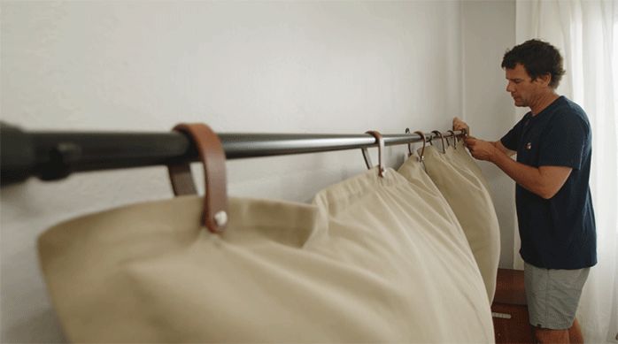 un hombre cuelga las almohadas de color beige en la barra de cortina que está fija en el muro del dormitorio.