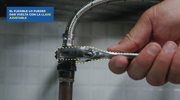 un hombre enrosca el flexible del monomando en la cañería de agua, usando una llave ajustable.