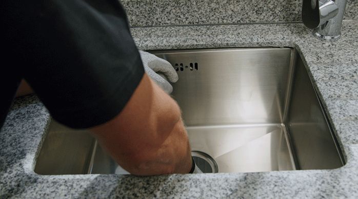 un hombre pega el lavaplatos bajo cubierta en la cubierta de granito.