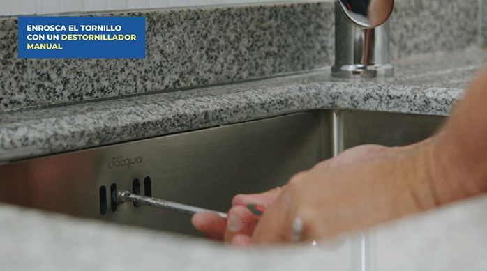 una persona fija la rejilla del desagüe en el lavaplatos bajo cubierta.