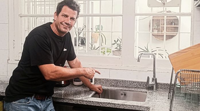un hombre mostrando el lavaplatos bajo cubierta que acaba de instalar en una cubierta de granito, en una linda cocina.