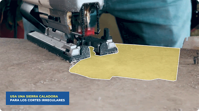una persona usa una sierra caladora para cortar una forma irregular en el piso vinílico SPC.