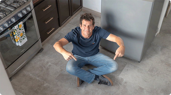 un hombre sentado en el piso de una cocina que acaba de ser renovado con piso vinílico SPC.
