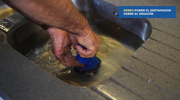 un hombre usa un destapador manual o un sopapo para destapar el desagüe de un lavaplatos.