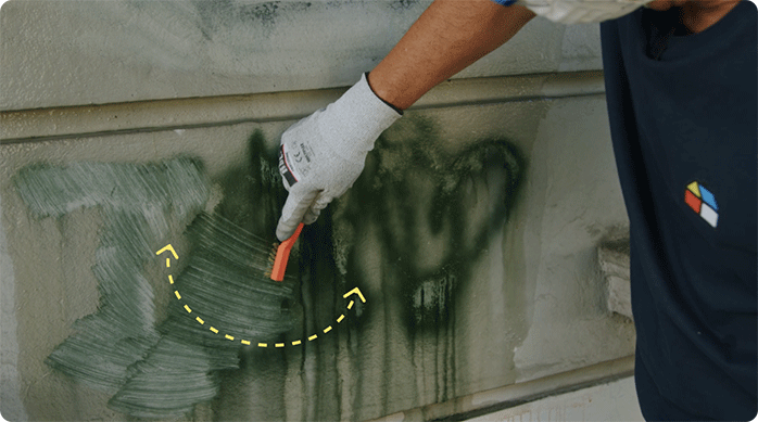 una persona con mascarilla y guantes de seguridad pasa una escobilla con cerdas de acero para remover aún más rápido el rayado del muro.
