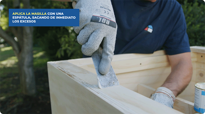 una persona aplica pasta de retape en los agujeros de los tornillos en la mesa de centro.