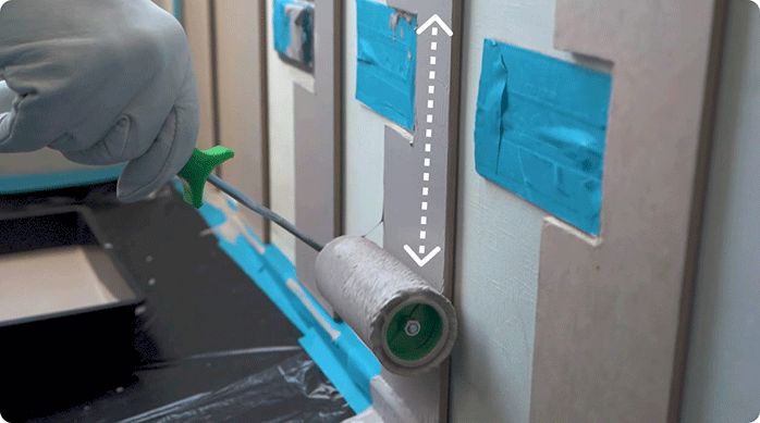 una persona pinta el muro de un dormitorio que tiene listones de mdf recién pegados.