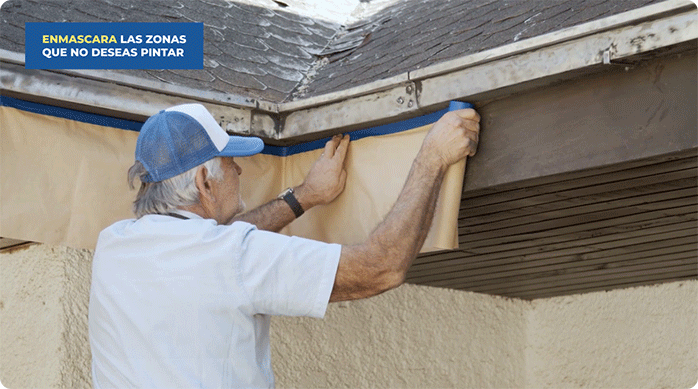 un hombre pone un protector para pintar en el borde de las canaletas de una casa.