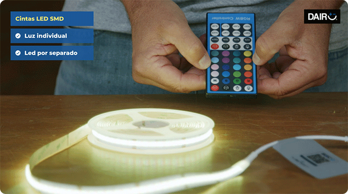 una persona sostiene el control remoto de una tira de luces led frente a la cinta.