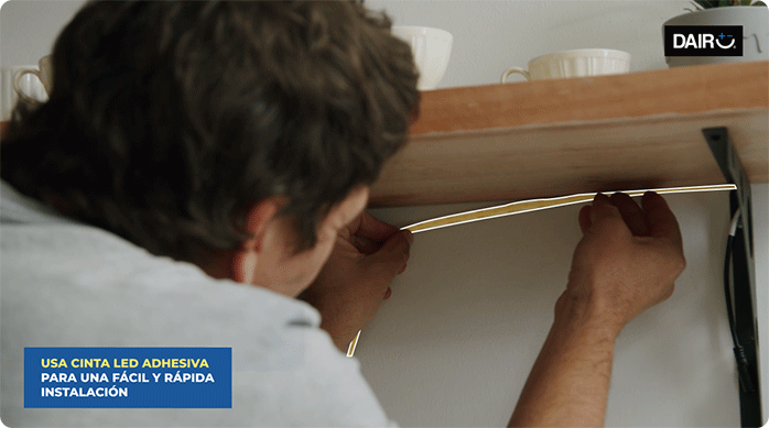 un hombre pega una cinta de luces led bajo la repisa de una cocina.