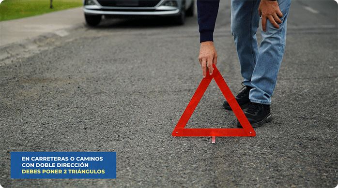 una persona pone un triángulo reflectante en medio de la calle, donde acaba de estacionar.
