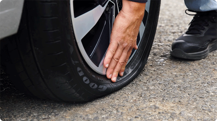 una persona usa su mano para revisar el neumático de un auto.