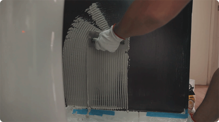 una persona aplica adhesivo para cerámica en la pared del baño.