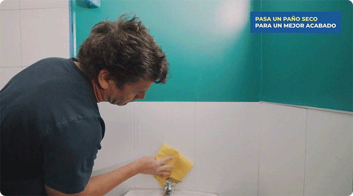 un hombre pasa un paño húmedo para limpiar el muro de cerámica del baño.