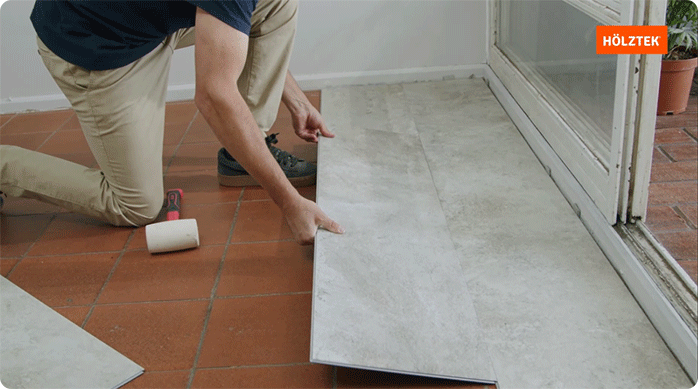 una persona instala piso vinílico en el piso de un living, usando el sistema clic.