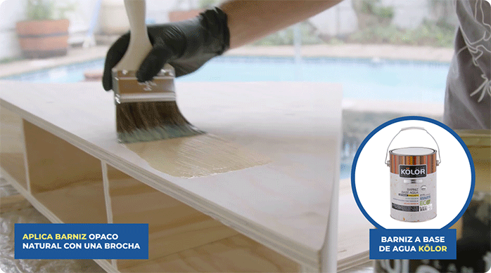 una persona aplica barniz a base de agua Kölor con una brocha sobre toda la superficie del mueble esquinero.