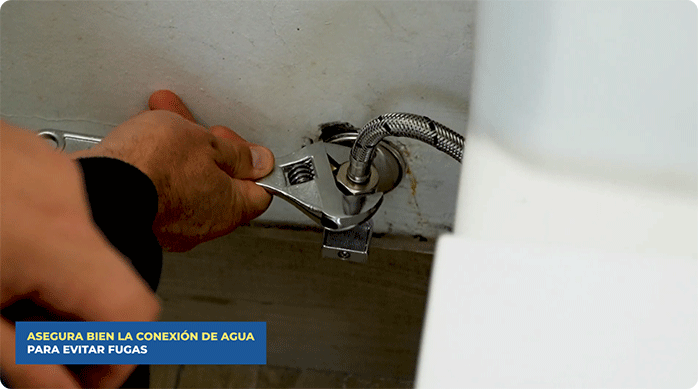 una persona atornilla el flexible del WC a la llave de paso.