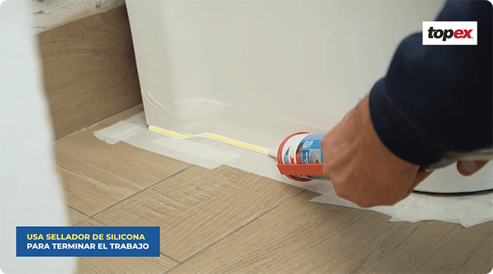 una persona sella el borde entre la taza y el piso usando silicona.