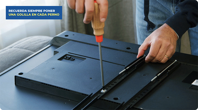 un hombre fija el soporte en la parte posterior de la tv con tornillos y un desatornillador manual.