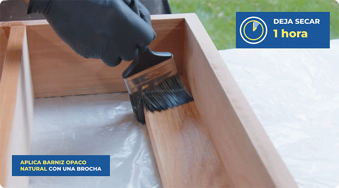 una persona aplica barniz opaco natural en el mueble estante para baño pequeño usando una brocha.