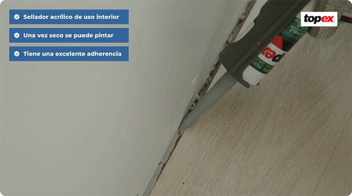 una persona aplica sellador acrílico con una pistola calafatera en el borde del piso vinílico adhesivo.