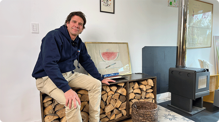 un hombre sentado en el nuevo leñero interior que acaba de construir para mantener la leña dentro de casa, al lado de su chimenea.