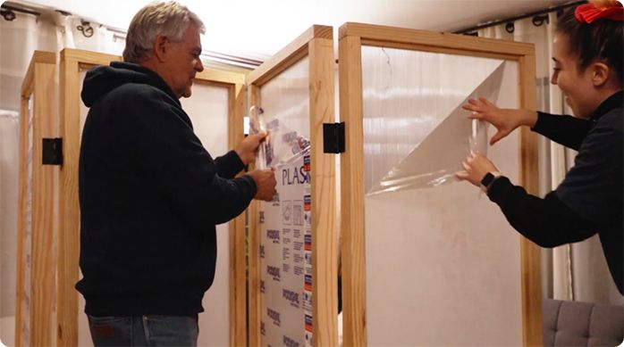 un hombre y una mujer retiran el plástico protector de las planchas de policarbonato del biombo.