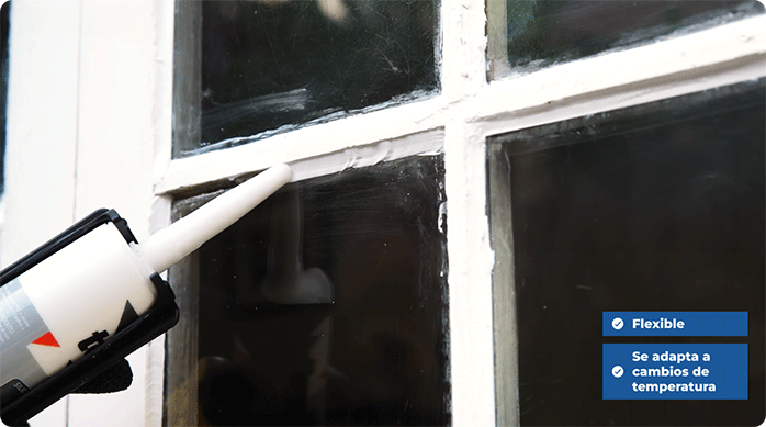 una persona aplica silicona neutra en la ventana para sellar los vidrios, usando una pistola calafatera.